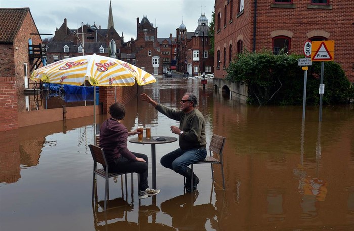 Trong màn nước lụt của sông Ouse, những người đàn ông ngồi uống bia bên ngoài quán bar ở York, Anh ngày 26/9. Ngập lụt sau hai ngày mưa lớn đã khiến hàng trăm người phải sơ tán khỏi nhà.